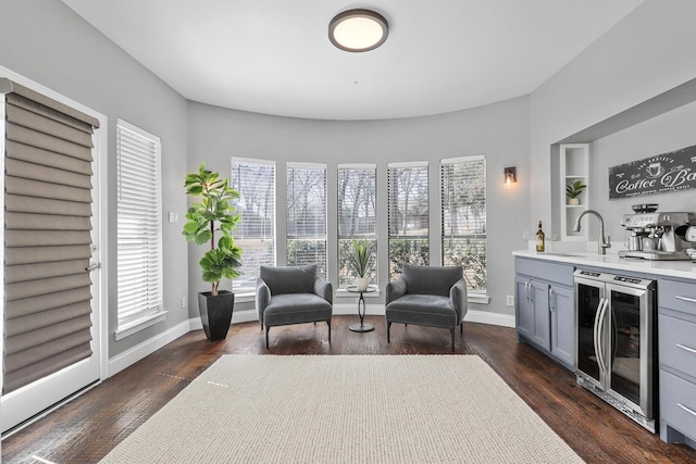 sitting room featuring beverage cooler, wet bar, baseboards, and dark wood finished floors