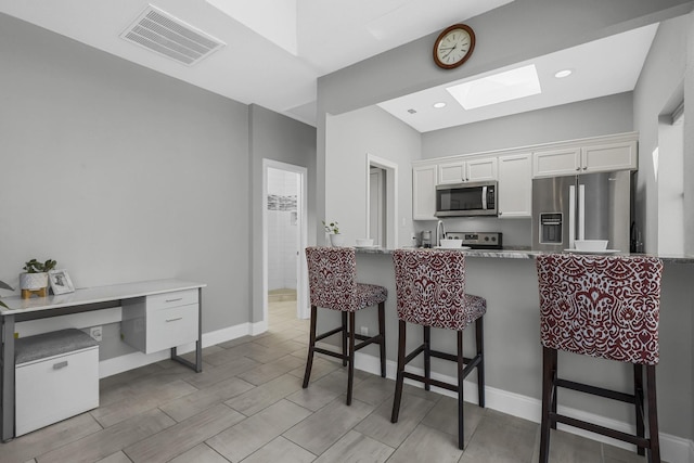 kitchen featuring stainless steel appliances, a breakfast bar, a skylight, visible vents, and white cabinetry