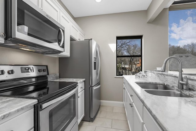 kitchen with light tile patterned floors, light stone countertops, stainless steel appliances, white cabinetry, and a sink