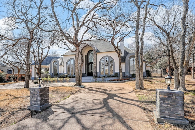 view of front of home featuring driveway, a chimney, and stucco siding