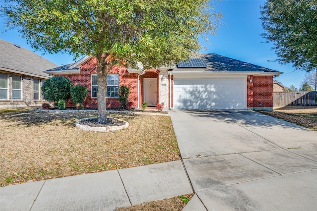 single story home with brick siding, an attached garage, fence, and roof mounted solar panels