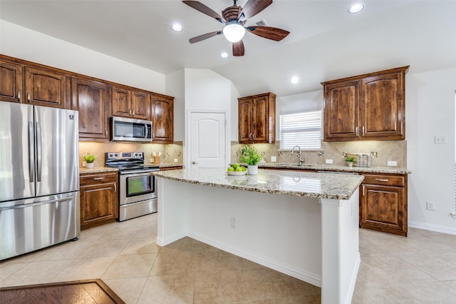 kitchen with light tile patterned floors, appliances with stainless steel finishes, a center island, light stone countertops, and a sink