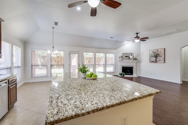 kitchen with visible vents, light stone countertops, white dishwasher, vaulted ceiling, and a fireplace