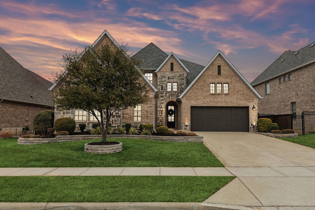 french country inspired facade featuring brick siding, fence, driveway, stone siding, and a lawn