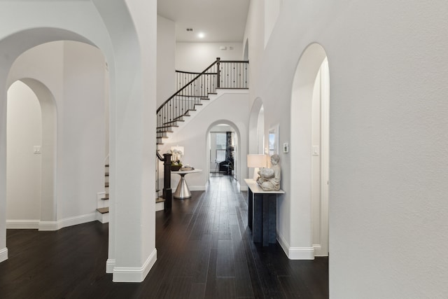 entrance foyer featuring baseboards, arched walkways, a towering ceiling, wood finished floors, and stairs