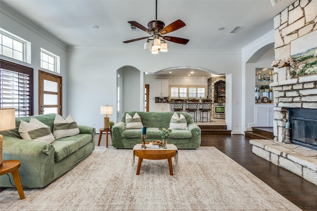 living area with a fireplace, visible vents, wood finished floors, and ornamental molding