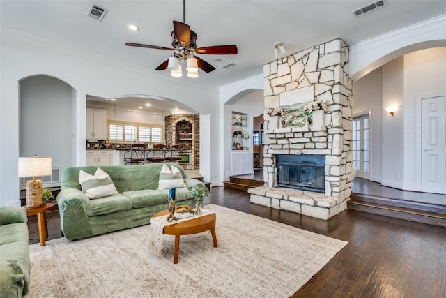 living area with a stone fireplace, visible vents, wood finished floors, and ornamental molding