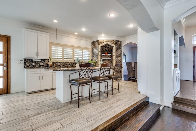 kitchen featuring backsplash, light wood-style floors, ornamental molding, white cabinets, and a kitchen breakfast bar