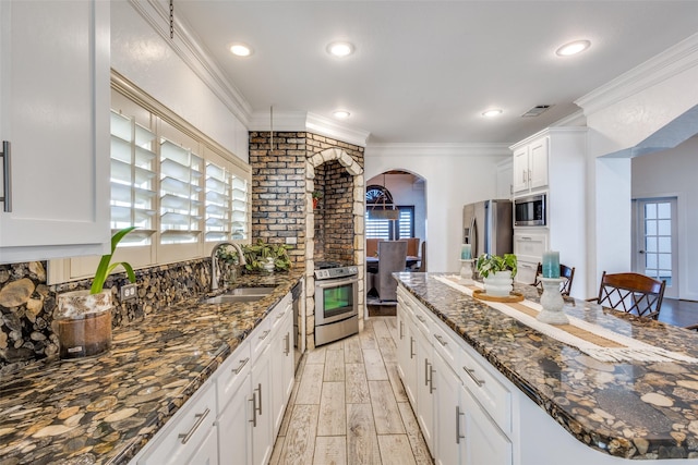 kitchen with arched walkways, appliances with stainless steel finishes, wood tiled floor, crown molding, and a sink