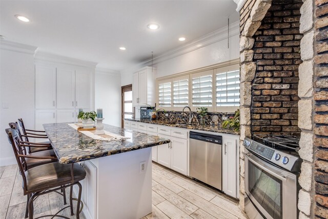 kitchen with white cabinets, dark stone counters, a center island, stainless steel appliances, and crown molding