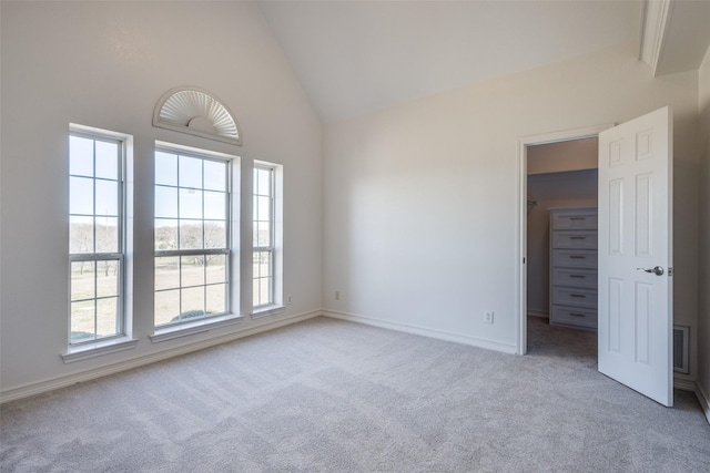 empty room featuring high vaulted ceiling, light colored carpet, visible vents, and baseboards