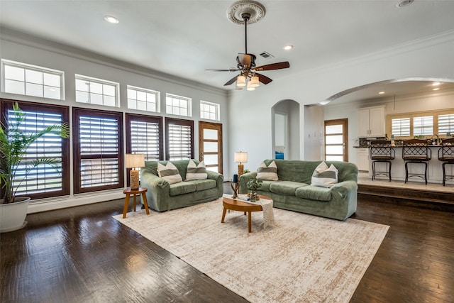 living area with a wealth of natural light, arched walkways, dark wood-style flooring, and crown molding