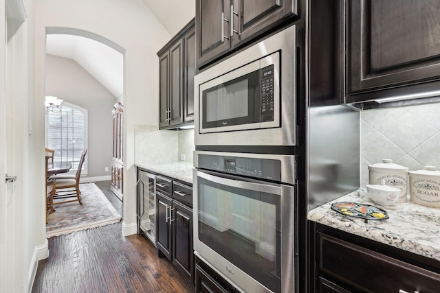 kitchen featuring beverage cooler, lofted ceiling, dark wood-style floors, appliances with stainless steel finishes, and light stone counters