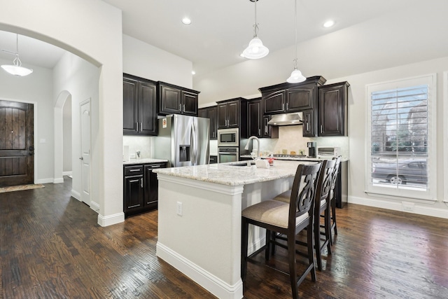 kitchen with arched walkways, dark wood-style flooring, stainless steel appliances, under cabinet range hood, and a sink