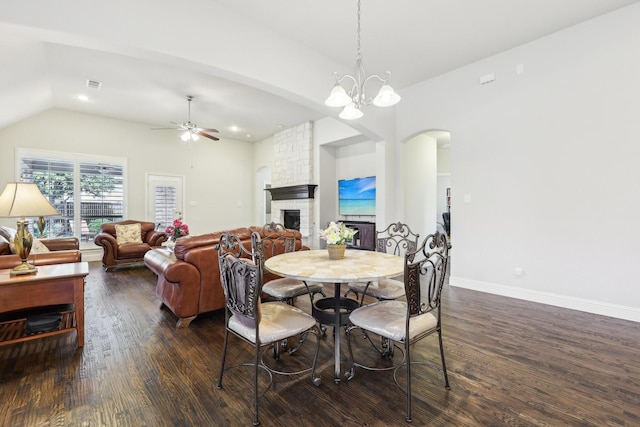 dining room featuring arched walkways, lofted ceiling, a stone fireplace, dark wood-type flooring, and visible vents