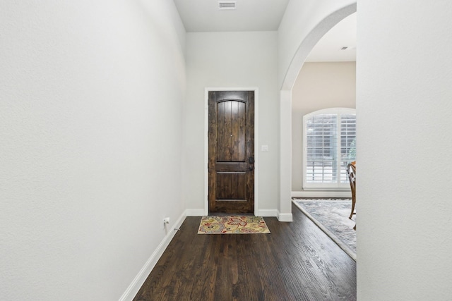 foyer entrance featuring baseboards, arched walkways, and wood finished floors