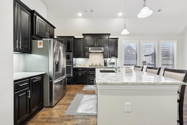 kitchen with stainless steel appliances, a sink, under cabinet range hood, and a kitchen bar