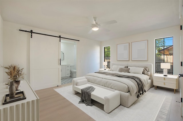 bedroom with ceiling fan, connected bathroom, light wood-style flooring, and a barn door