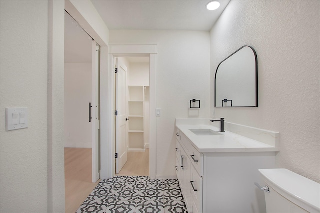 bathroom with toilet, a textured wall, a walk in closet, and vanity