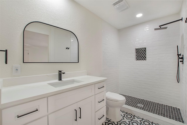 bathroom featuring visible vents, tiled shower, vanity, and toilet