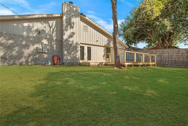 rear view of property with board and batten siding, fence, a lawn, and french doors