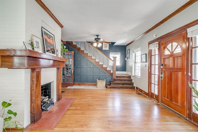 entryway featuring wood finished floors, baseboards, stairway, a brick fireplace, and crown molding