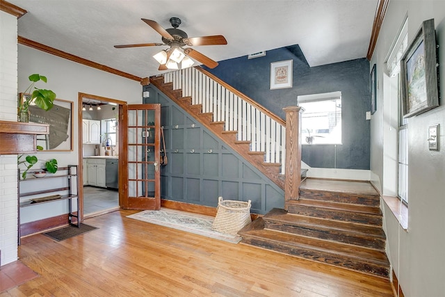 stairs featuring baseboards, visible vents, a ceiling fan, hardwood / wood-style floors, and crown molding