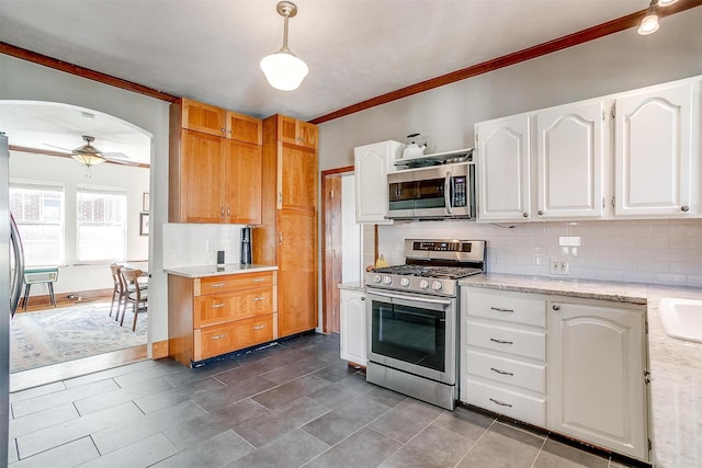 kitchen featuring arched walkways, a ceiling fan, white cabinetry, appliances with stainless steel finishes, and backsplash