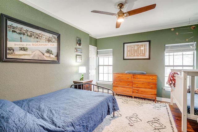 bedroom featuring a textured wall, ornamental molding, ceiling fan, wood finished floors, and baseboards