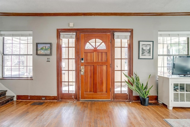 foyer with ornamental molding, wood-type flooring, visible vents, and stairway