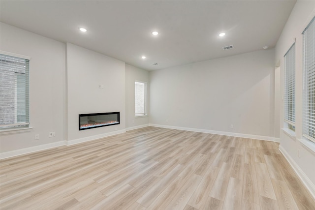 unfurnished living room featuring recessed lighting, visible vents, baseboards, light wood-type flooring, and a glass covered fireplace