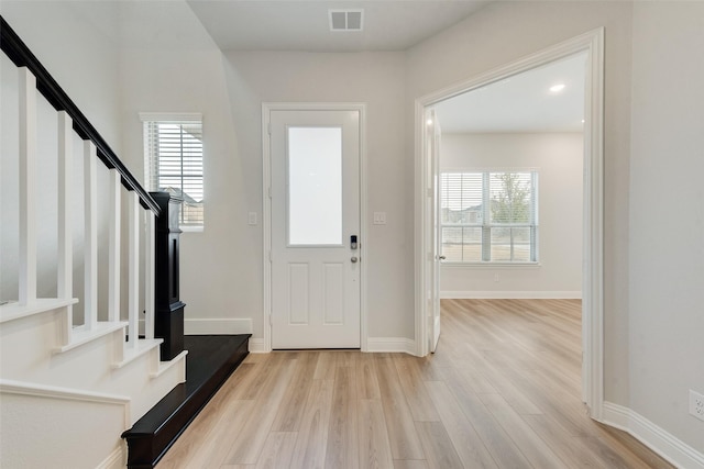 foyer with light wood-style floors, baseboards, stairway, and visible vents