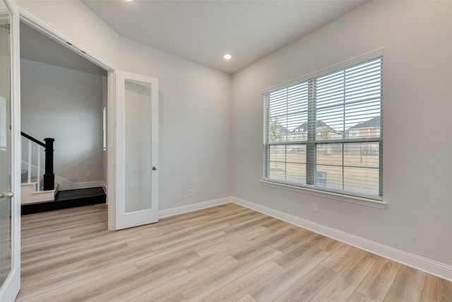 empty room with light wood-style floors, stairway, and baseboards