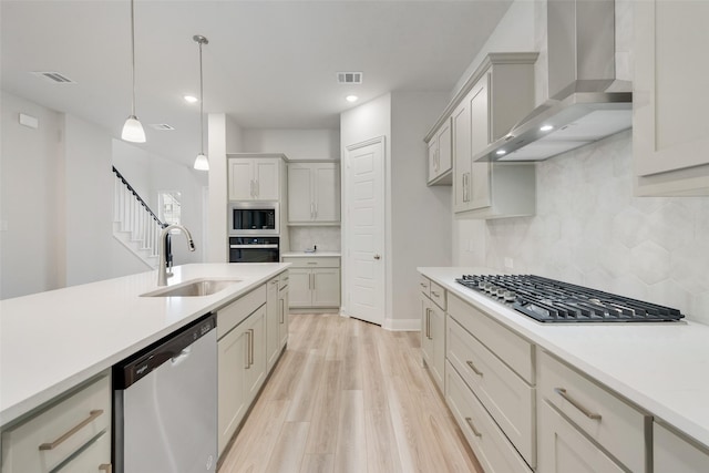 kitchen featuring visible vents, appliances with stainless steel finishes, light countertops, wall chimney range hood, and a sink