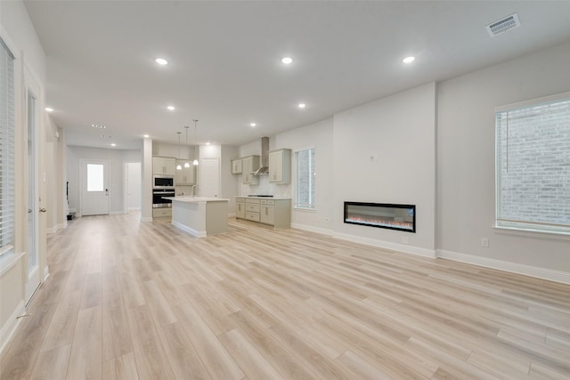 unfurnished living room featuring light wood-style floors, a glass covered fireplace, visible vents, and recessed lighting