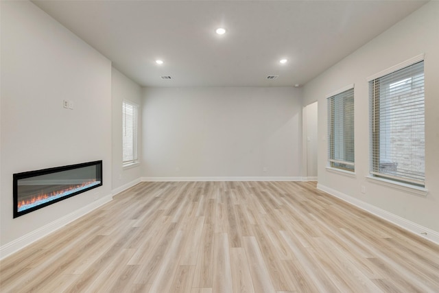 unfurnished living room featuring light wood-style floors, a glass covered fireplace, a wealth of natural light, and baseboards