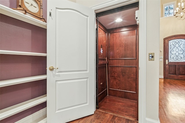 interior space with elevator, wood finished floors, and an inviting chandelier