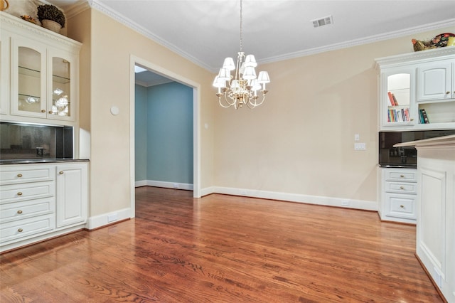 unfurnished dining area with baseboards, wood finished floors, visible vents, and crown molding