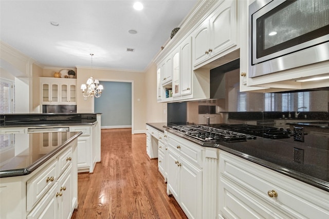 kitchen with appliances with stainless steel finishes, dark countertops, white cabinets, and crown molding