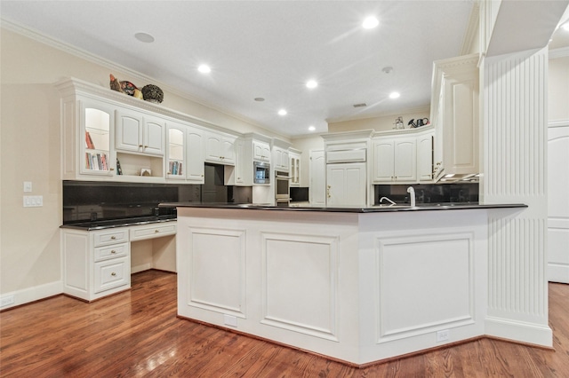 kitchen featuring built in study area, dark countertops, ornamental molding, wood finished floors, and a peninsula