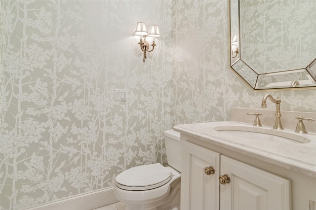 bathroom with vanity, toilet, and wallpapered walls