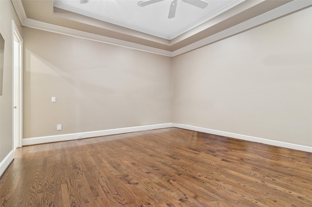 empty room with a tray ceiling, ornamental molding, wood finished floors, and baseboards