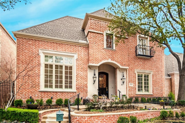 view of front facade with a shingled roof, brick siding, and a balcony