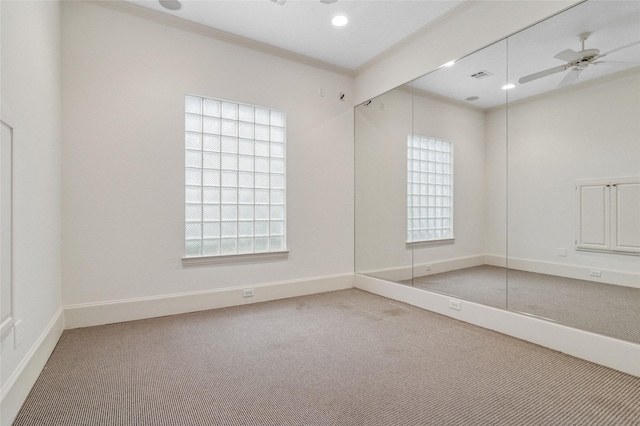 carpeted empty room with ceiling fan, plenty of natural light, visible vents, and crown molding