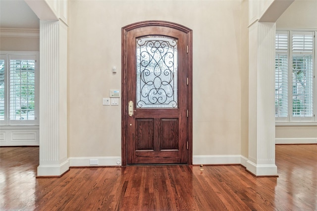 foyer entrance featuring baseboards, wood finished floors, decorative columns, and crown molding