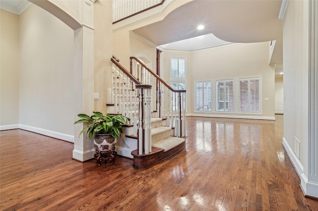 entrance foyer with a towering ceiling, baseboards, ornamental molding, and hardwood / wood-style floors