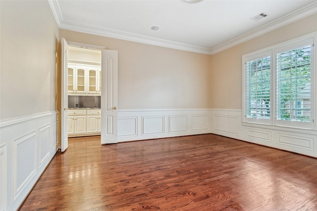 unfurnished room featuring a wainscoted wall, ornamental molding, a decorative wall, and wood finished floors