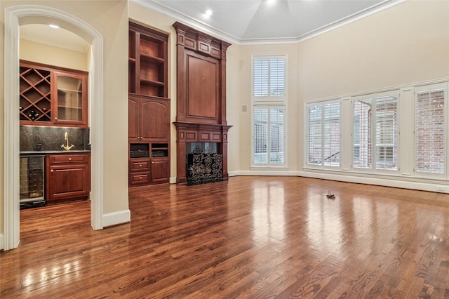 unfurnished living room featuring beverage cooler, dark wood-style flooring, wet bar, crown molding, and a high end fireplace