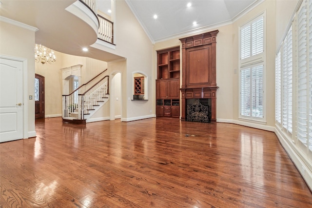 unfurnished living room with a fireplace, stairway, a towering ceiling, ornamental molding, and wood finished floors