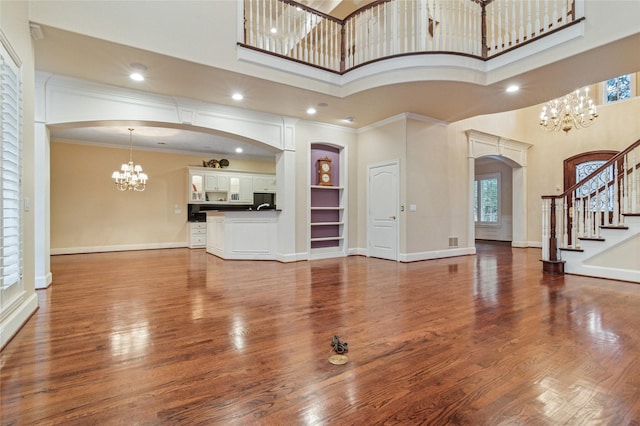 unfurnished living room with a chandelier, arched walkways, wood finished floors, baseboards, and stairs